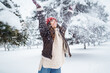 Happy woman in a red hat and scarf plays with snow in a winter park. Concept of relaxation, fun.