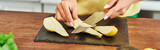 Fototapeta Kosmos - cropped view of vegetarian woman cutting ripe pear on chopping board in kitchen, horizontal banner