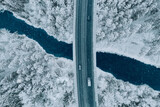 Fototapeta Na ścianę - Aerial top view of snow winter road with cars over blue river