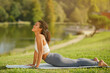 Fit lady practicing cobra pose on yoga mat outdoors