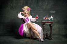 Serious Princess, Aristocratic Medieval Person In Old-fashioned Dress And Modern Shoes Sitting Holding Cocktail Against Vintage Background.