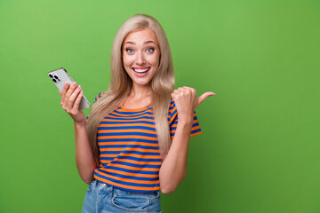 Sticker - Photo of excited cheerful girl wearing stylish clothes presenting empty space novelty device shop isolated on green color background