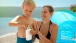Portrait of little baby boy with mother applying sunscreen UV protection lotion on sea beach during summer holiday vacation