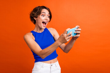 Canvas Print - Photo of pretty overjoyed lady hold smart phone have fun playing video games isolated on orange color background