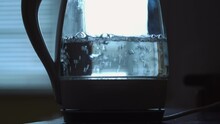 Transparent kettle with boiling water on the background of the window. The concept of a coffee break and the end of the working day.