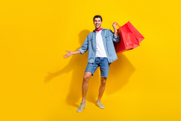 Poster - Full size photo of satisfied cheerful guy wear jeans jacket holding shopping bags buy new clothes isolated on yellow color background