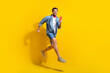 © deagreez - Full size photo of excited positive guy wear jeans jacket scarf run shopping holding smartphone in arm isolated on yellow color background