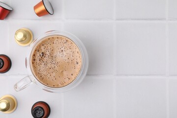 Canvas Print - Cup of coffee and capsules on white tiled table, flat lay. Space for text