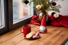 Holidays, Decoration And Celebration Concept - Close Up Of Christmas Gnome, Cup Of Coffee In Red Mug, Ginger Cookies And Candy Canes On Window Sill At Home