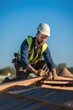 © Stavros - A male roofer is in the process of strengthening the wooden structures of the roof of a house. A middle-aged Caucasian man is working on the construction of a wooden frame house. Vertical photo.