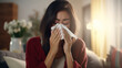 Young woman with a cold blowing her nose into a tissue, cozy at home with warm lighting