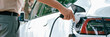 Leinwandbild Motiv Young man recharge electric car's battery from charging station in outdoor green city park. Rechargeable EV car for sustainable environmental friendly urban travel. Panorama Expedient