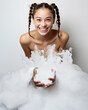 © J S - Cosmetics portrait of a happy sweet young brunette woman smile and playing with bath foam as spa fun, pigtail hairstyle, copy space on white walls
