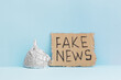 Aluminium foil hat and fake news poster on blue background, symbol for conspiracy theory and mind control protection. Top view