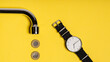 concept. metal tap spout on a yellow background, Polish zloty coins arranged in a row, and a watch with a white dial lying next to it. bright yellow image