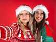 © Designerant - Happy noel time. Portrait of beautiful fun two female friends hug and embrace in santa's hat wear knitted Christmas sweater. Doing selfie shot, memories of December winter feast concept idea.