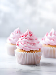 Wall Mural - Delicious vanilla cupcakes with pink frosting on top, white marble table with blurry bright background