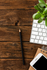 Office desktop with computer keyboard, smart phone, notebook, pen and green plant on wooden table. Business background