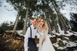 A young couple, the bride and groom, smilingly show off their wedding rings against the background of tall trees. Have a good time laughing. Winter wedding