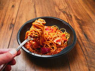 Spaghetti Bolognese on a metal fork and in black plastic container on wooden table. Premium, high quality traditional Italian style ready meal. Fast food product for mass consumption. 