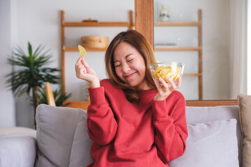 Wall Mural - Portrait image of a happy woman picking and eating potato chips at home