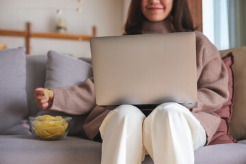 Wall Mural - Closeup image of a young woman eating potato chips while using laptop at home