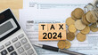 Word Tax 2024 in the wooden cube. US Individual income tax return. US tax forms and glass coin jar with calculator on desk . tax 1040. Government, state taxes. Calculation tax return. Accounting.
