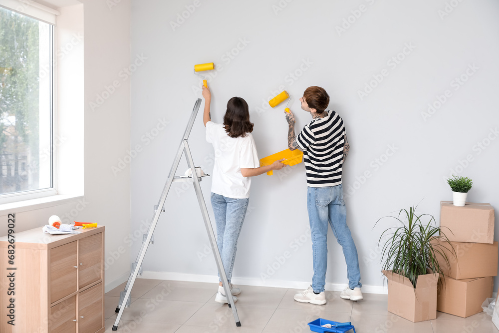 Young couple painting wall with rollers in their new house, back view