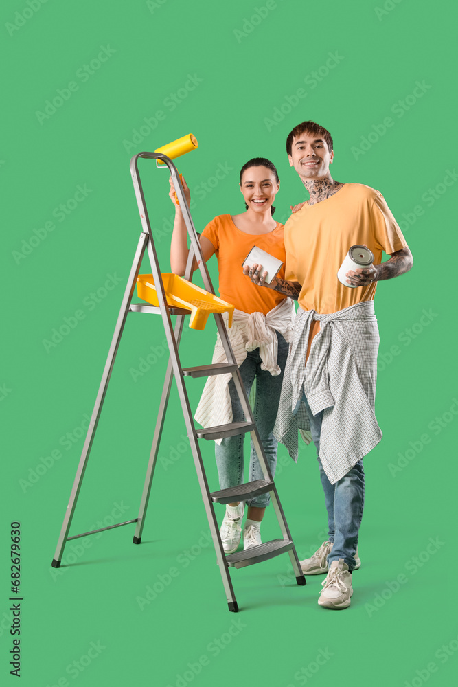 Young couple with paint cans and roller on green background
