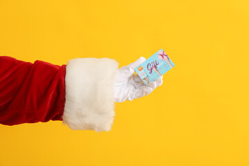 Sticker - Santa Claus hand with gift card on yellow background, closeup