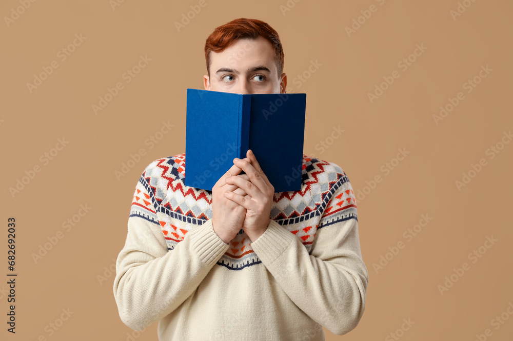 Young man clothing face with book on color background