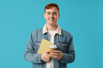 Wall Mural - Young man holding book and cup of coffee on color background