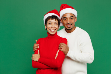 Wall Mural - Merry smiling lovely young couple friends man woman wearing red casual clothes Santa hat posing looking camera hugging isolated on plain green background Happy New Year 2024 Christmas holiday concept