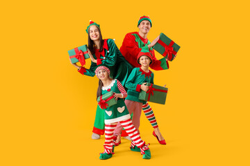 Poster - Happy family in elf's costumes with gift boxes on yellow background