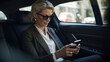 Mature businesswoman reading text message on her cell phone while traveling in a cab - Generative AI