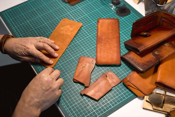 Wall Mural - man cutting leather with knife for sewing a wallet. close up cropped shot. Leather work. Tools for sewing bags, wallets, clutches. Sewing products by hand. Manufacture of leather goods.