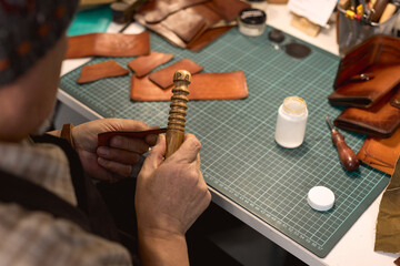 Wall Mural - closeup cropped photo back view craftsman working using edge slicker,accurate process of sewing, making wallet, purse, bag, lifestyle. man works with Leather Working Burnisher Slicker Tools