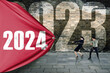 © Creativa Images - Two business people pulling a blue banner with numbers 2024 over 2023 numbers on the wall