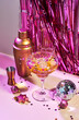Splash in champagne glass, cocktail glass, shaker, and jigger on pink table with Christmas decorations