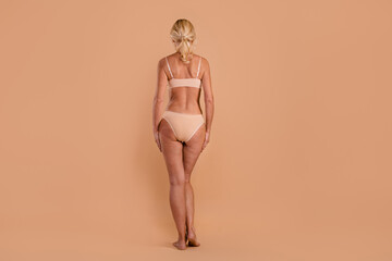 Poster - Full length photo of slim sexy middle age woman wear bikini standing back isolated beige color background