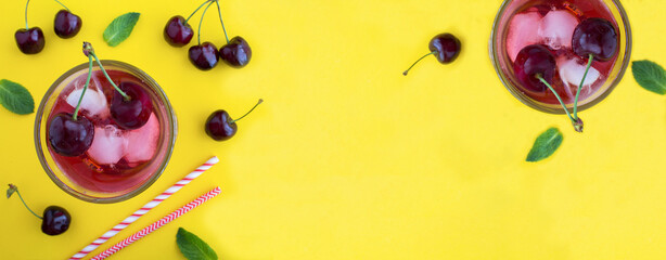 Wall Mural - Cold lemonade with cherries in the drinking glass on the yellow background. Top view. Copy space.