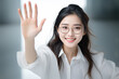 © Surachetsh - Stylish young Asian with glasses and long hair, clad in a crisp white shirt, confidently raises a hand, palm out, against a blurred technology backdrop. Generative AI.