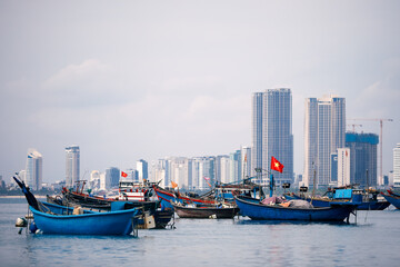 Wall Mural - Selective focus on Vietnamese flag on fishing boat moored in port against coast with modern buildings. Da Nang cityscape in Vietnam..
