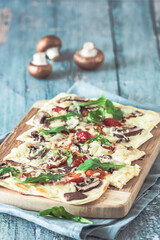 Wall Mural - Freshly baked flammkuchen, traditional french tarte flambee or german pizza in a vegetarian recipe with mushrooms, cream cheese, tomatoes and arugula, on light green wooden board and table