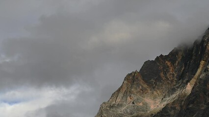 Wall Mural - time lapse of gray clouds moving across a prominent rocky mountain cliff. the rocks are in shades of