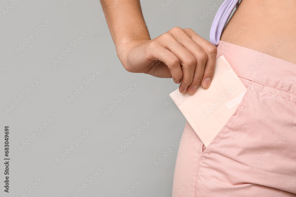 Beautiful young woman with menstrual pad on grey background