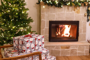 Wall Mural - Merry Christmas! Stylish wrapped christmas gifts on arm chair against christmas tree with festive lights and cozy burning fireplace. Atmospheric Christmas eve, holiday time.