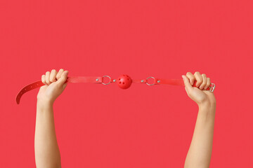 Female hands with mouth gag from sex shop on red background, closeup