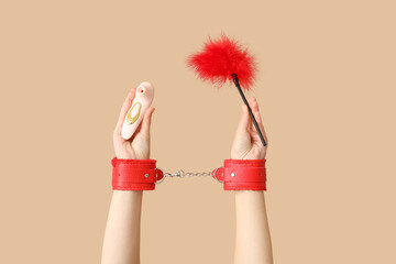 Woman in red handcuffs holding sex toys on color background, closeup