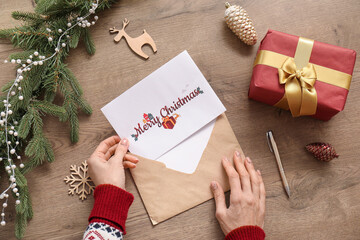 Wall Mural - Mature woman with greeting card for Christmas celebration in envelope on table, top view